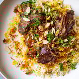 Garnished with fresh cilantro and almonds, the delicious Qatari Majboos is a flavorful Middle Eastern meal.