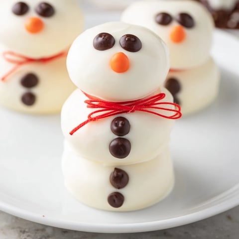 White chocolate-covered Express Snowman Marshmallow Pops, adorned with dark chocolate faces and orange noses.