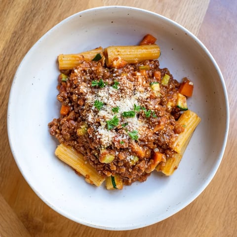 Steaming bowl of High-Fiber Lentil Bolognese, a hearty pasta dish with vibrant holiday garnishes.