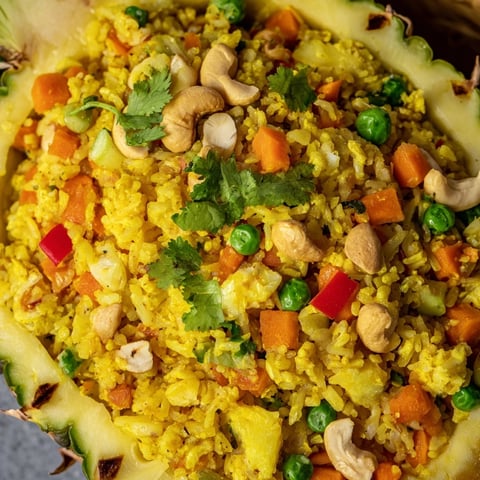 Fresh Pineapple Fried Rice is served in a hollowed-out pineapple shell, garnished with cilantro and lime wedges.