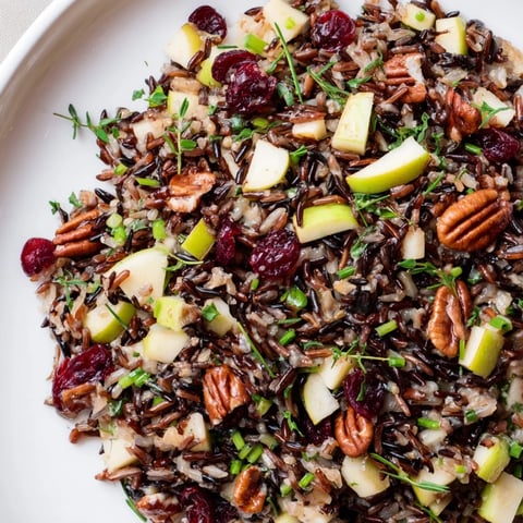 A close-up view of a vibrant Wild Rice Harvest Salad showcasing toasted pecans, dried cranberries, and fresh herbs in a rustic bowl.