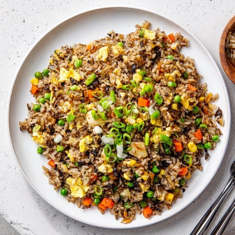 A close-up of vibrant Black Garlic Fried Rice, with glistening grains and colorful diced vegetables peeking through the savory mix.  