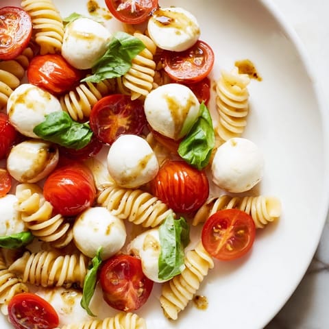 Close-up of a vibrant Caprese Pasta Salad, showing plump tomatoes and mozzarella with a balsamic glaze.
