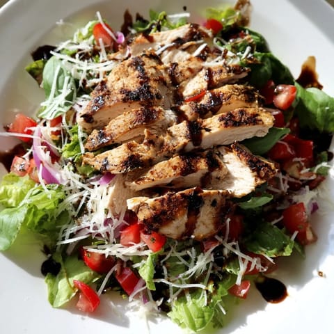 A close-up view of juicy grilled chicken on crisp romaine and arugula, generously drizzled with a zesty balsamic-tomato Bruschetta Chicken Salad mixture.
