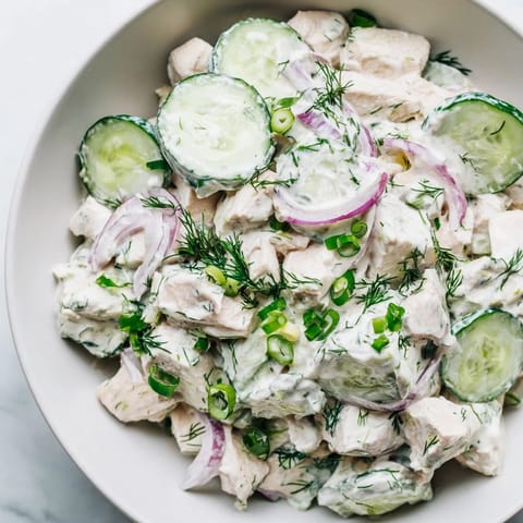Creamy cucumber chicken salad with Greek yogurt dressing, served chilled in a serving bowl topped with sliced green onions and red onion.