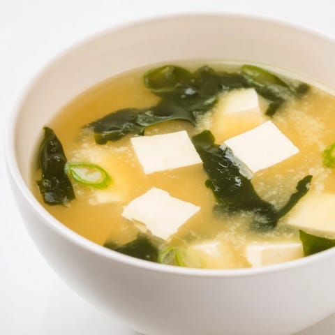 Steam rises from a cozy bowl of miso soup with tofu, garnished with fresh sliced scallions.