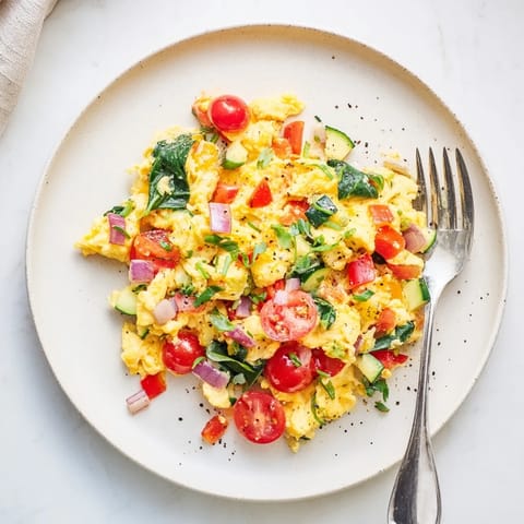 Fluffy egg and vegetable scramble served with avocado slices on a rustic plate for a colorful, nutritious breakfast.  