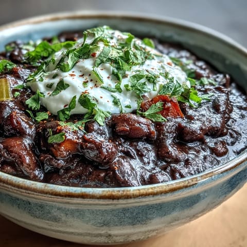 Spiced black bean soup with avocado and lime wedges, garnished with diced red onion for a fresh, zesty finish.