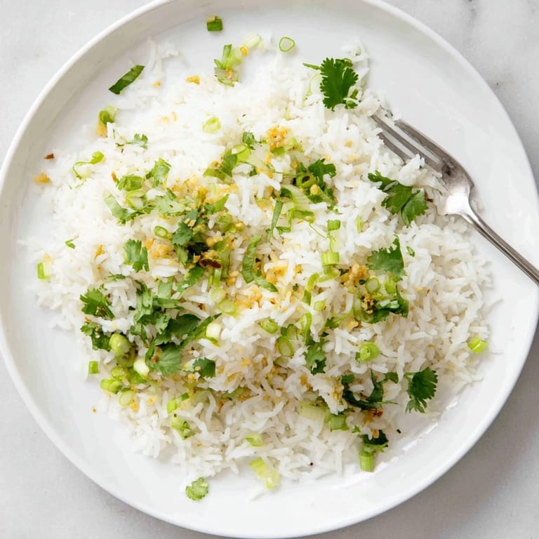 Garlic-infused jasmine rice with tender grains, prepared in a saucepan and garnished with vibrant green scallions.