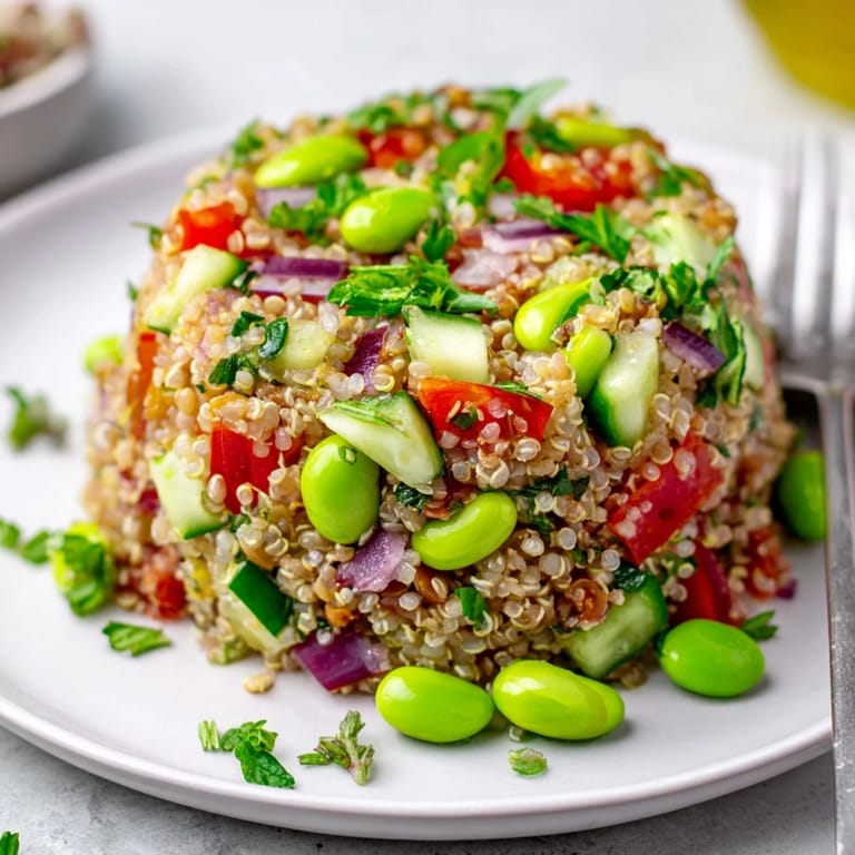 A chilled bowl of Edamame and Quinoa Salad showcases red bell pepper, cucumber, and cherry tomatoes, ideal for summer potlucks or sides.