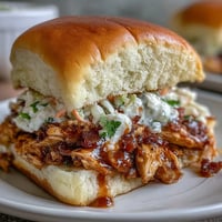 Savory shredded Mississippi chicken piled high on soft slider buns with tangy coleslaw for a crowd-pleasing party bite.  