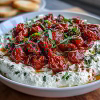 Whipped feta dip with roasted cherry tomatoes, garnished with fresh basil and olive oil, served with warm pita bread.  