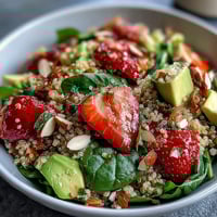 Vibrant strawberry avocado quinoa salad with fresh spinach, basil, and citrus dressing in a white bowl.  